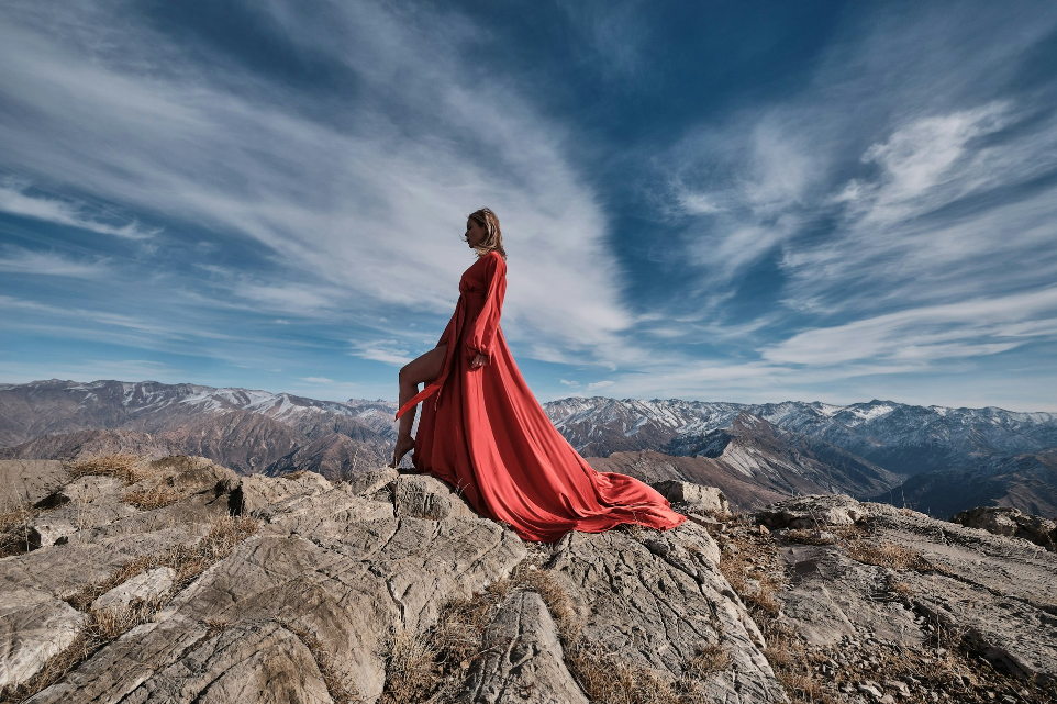 woman in red dress sitting on brown rock formation under blue sky during daytime